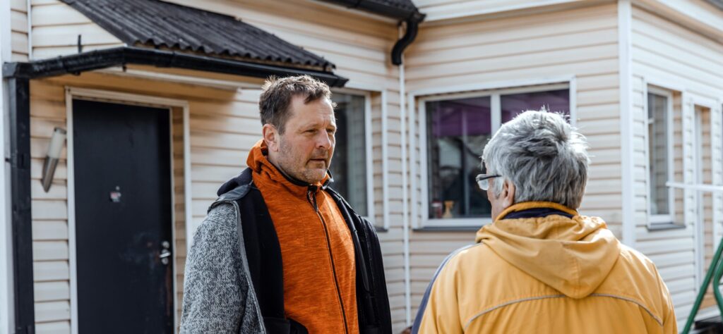 Een man spreekt met een oudere man bij de voordeur van een huis